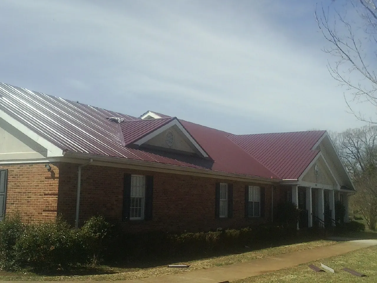 Red metal roof with gabled entries on a long brick building, from a Hail Damage Roof Repair job in Wetumpka