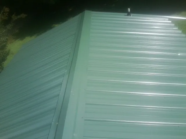 New green metal panels meeting at the ridge of a roof — Flat Roof Repair work by our crew in Wetumpka
