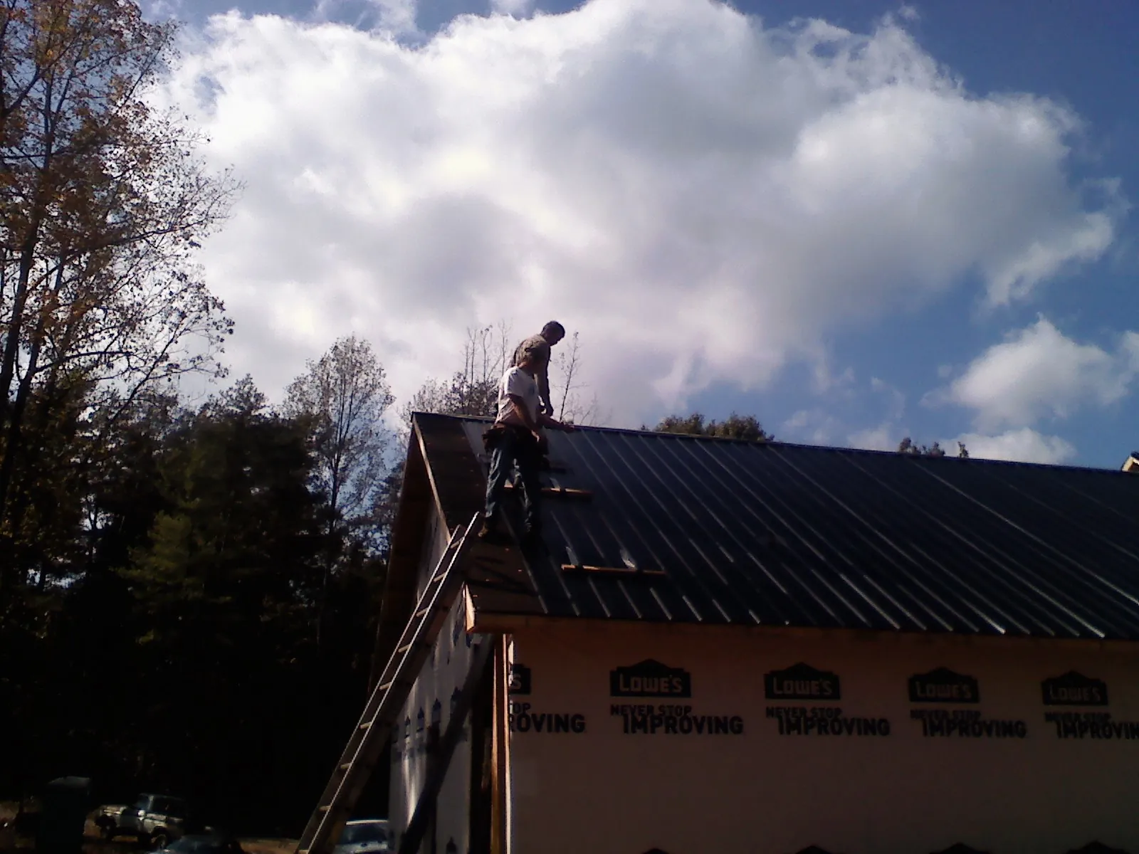 Roofer fastening dark metal panels high against a cloudy sky, from a Roof Inspection job in Wetumpka