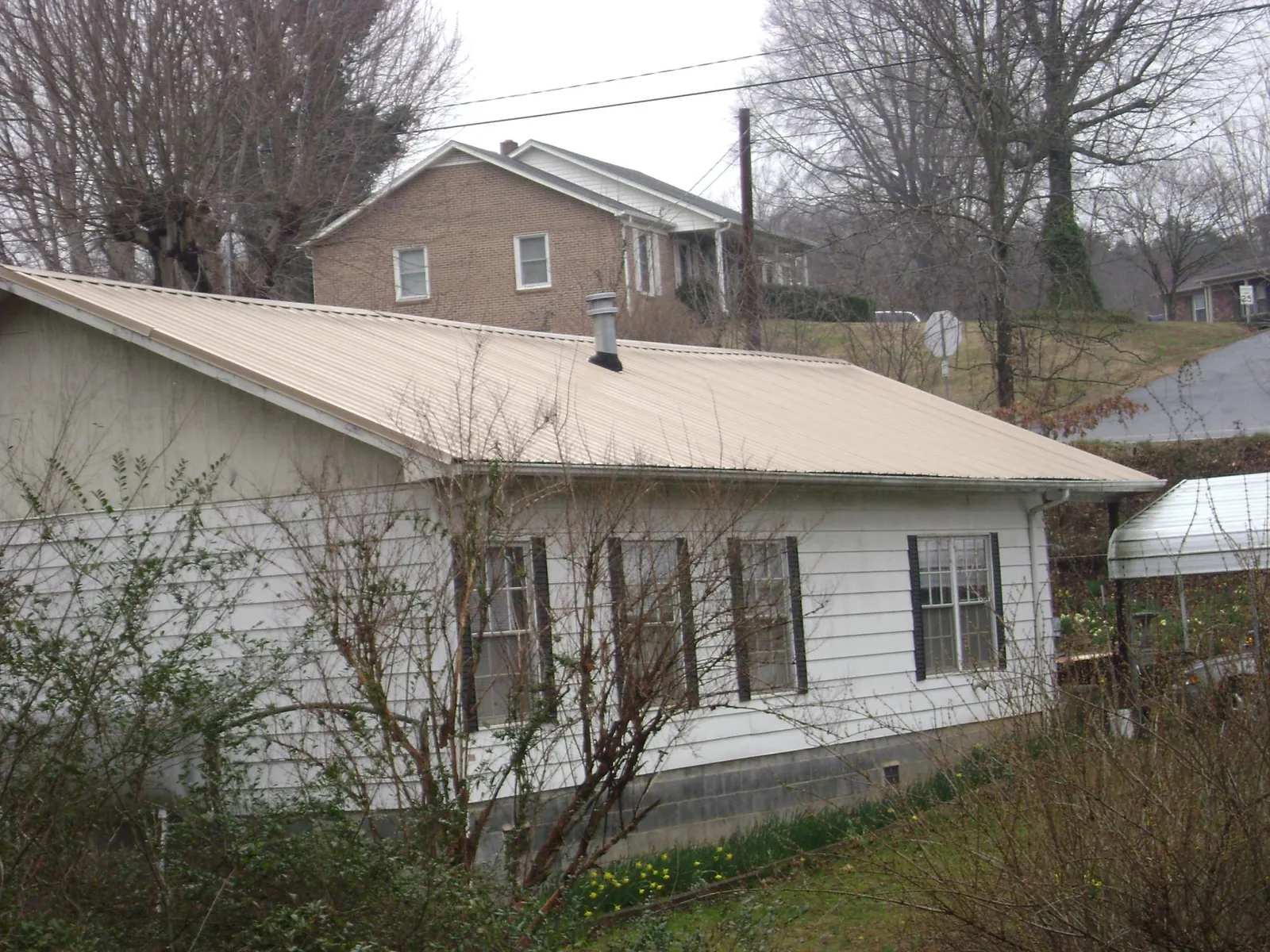 Tan metal roof on a white sided house set into a hillside — Commercial Roofing by Roofing Brothers in Wetumpka