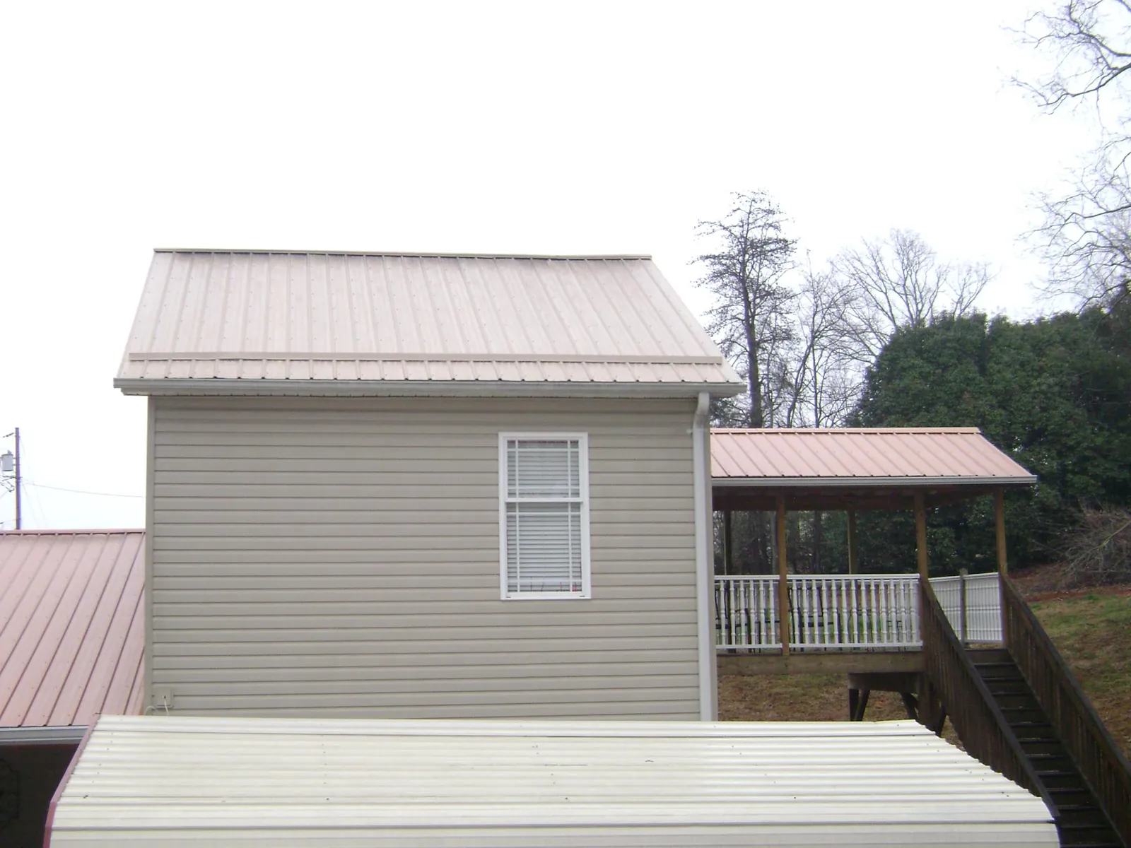 Tan metal roofs on a two story addition and attached porch, from a Roof Replacement job in Wetumpka